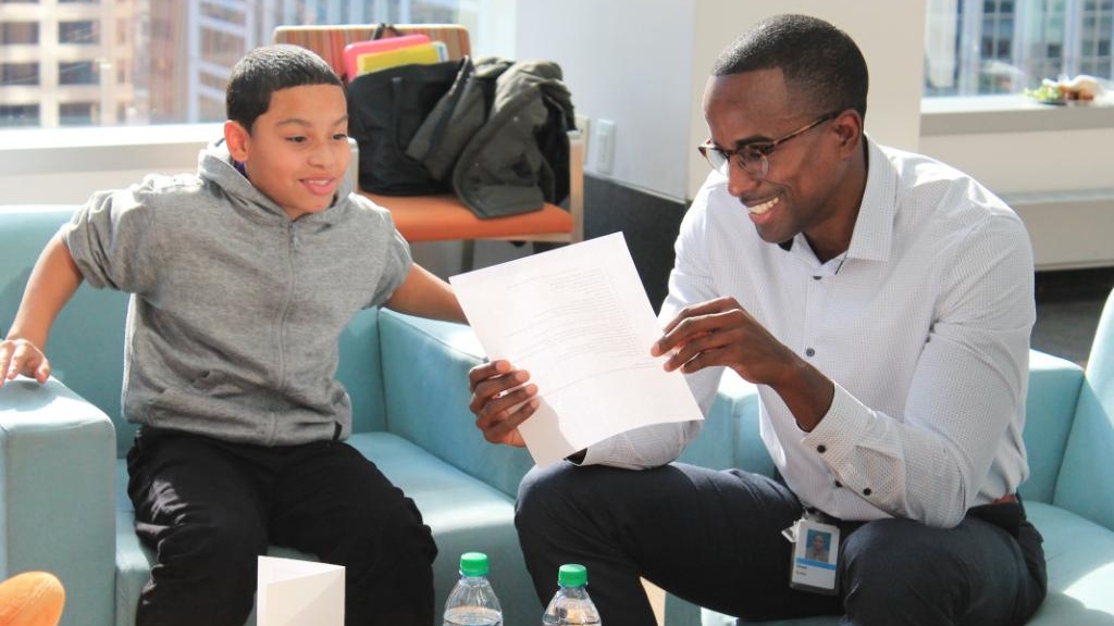 A Big Brother and Little Brother sit side by side and read a document together.