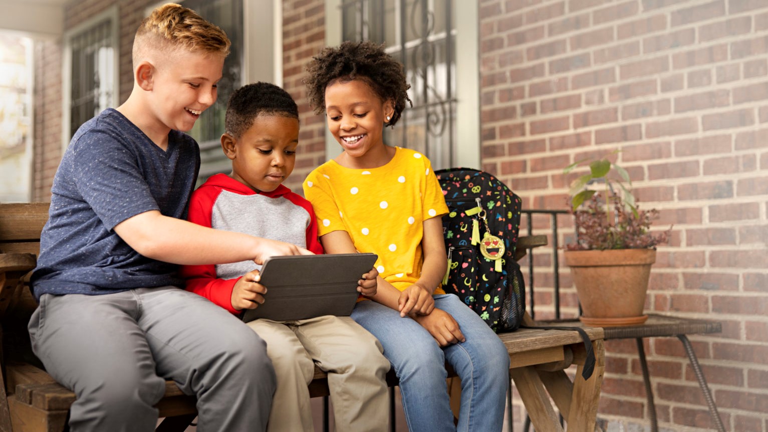 Three young students use a tablet to watch videos